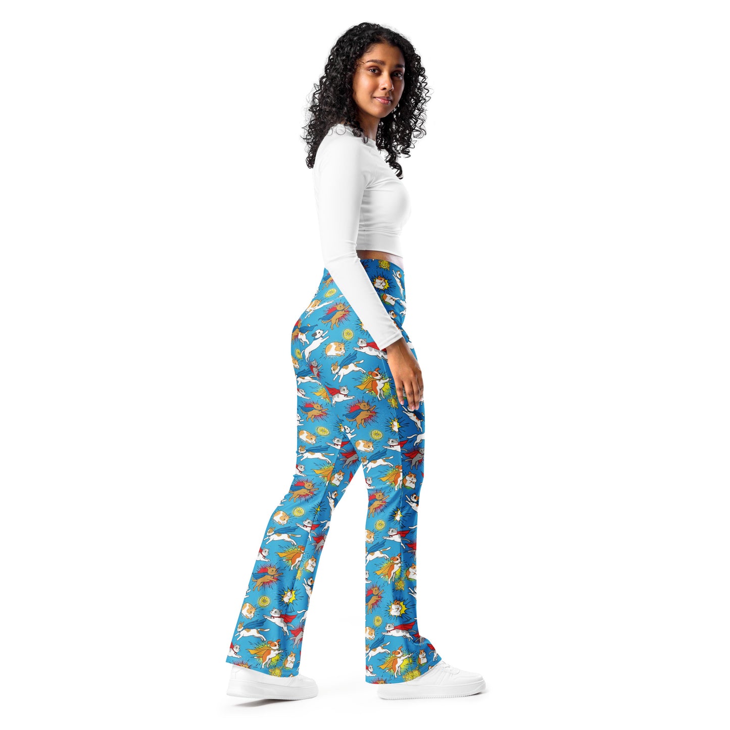 A woman modeling a pair of high-waisted, wide-leg pants with a colorful koi fish pattern on a blue background, paired with a white long-sleeve crop top and white sneakers, set against a plain white studio background. Bold Whimsical Superhero Pets Printed Flare Leggings Activewear