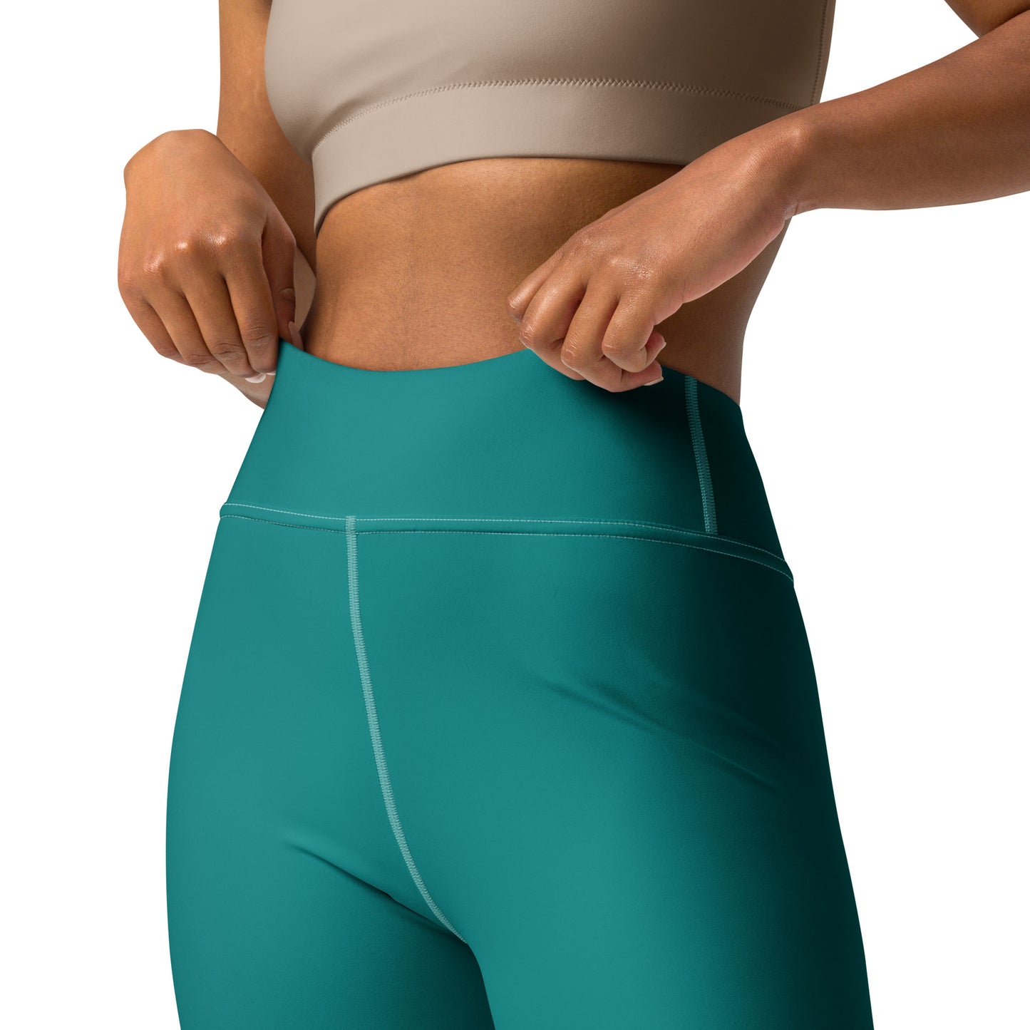 Close-up of a model wearing high-waisted teal athletic leggings, pulling the waistband slightly outward with both hands. The model is also wearing a beige sports bra, shown against a plain white background. Chic Comfortable Minimalist Plain Solid Color Teal Yoga Leggings for Activewear