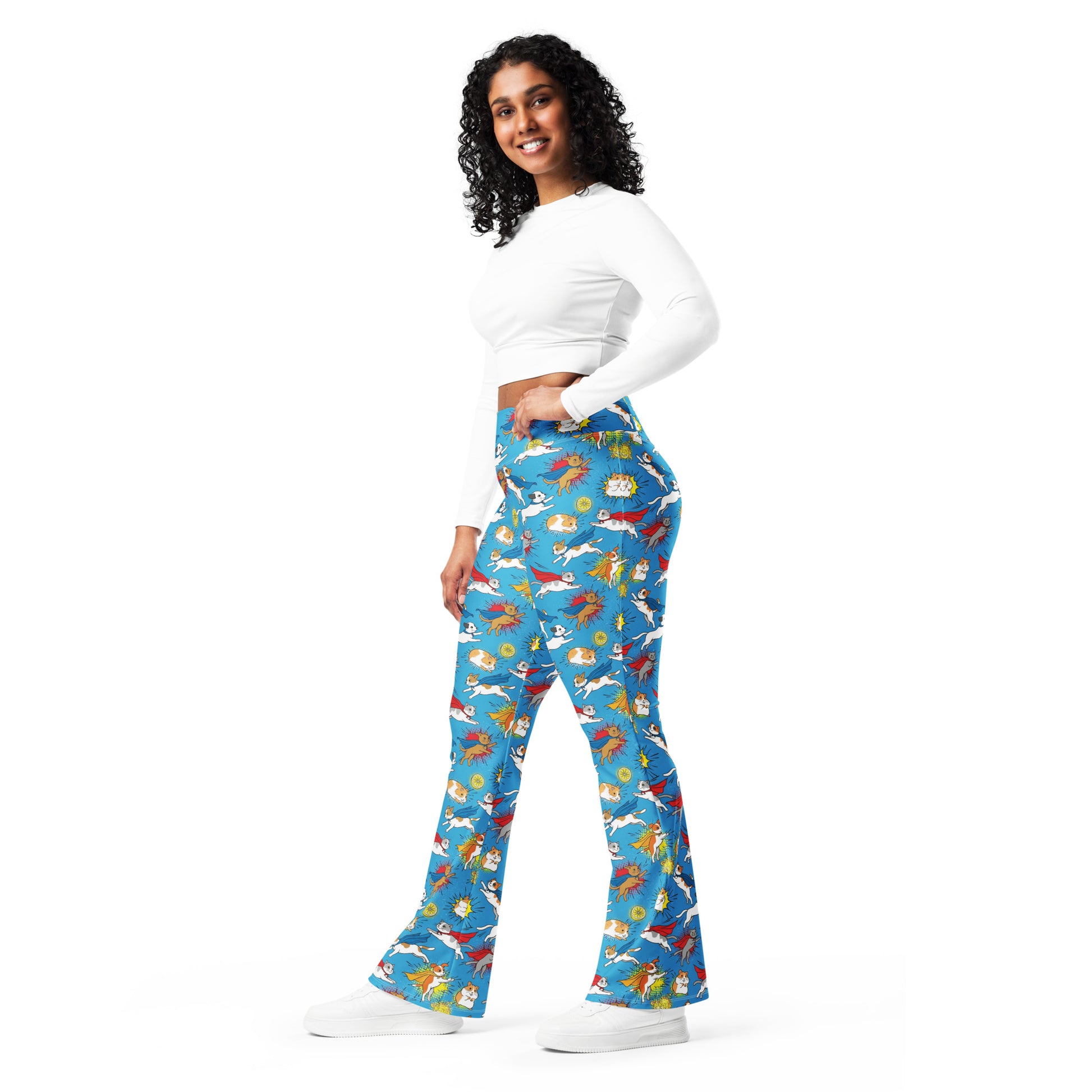 A woman modeling a pair of high-waisted, flared blue pants with a colorful cartoon fish pattern, paired with a white long-sleeve crop top and white sneakers, set against a plain white background. Adorable Whimsical Superhero Pets Printed Flare Leggings Activewear