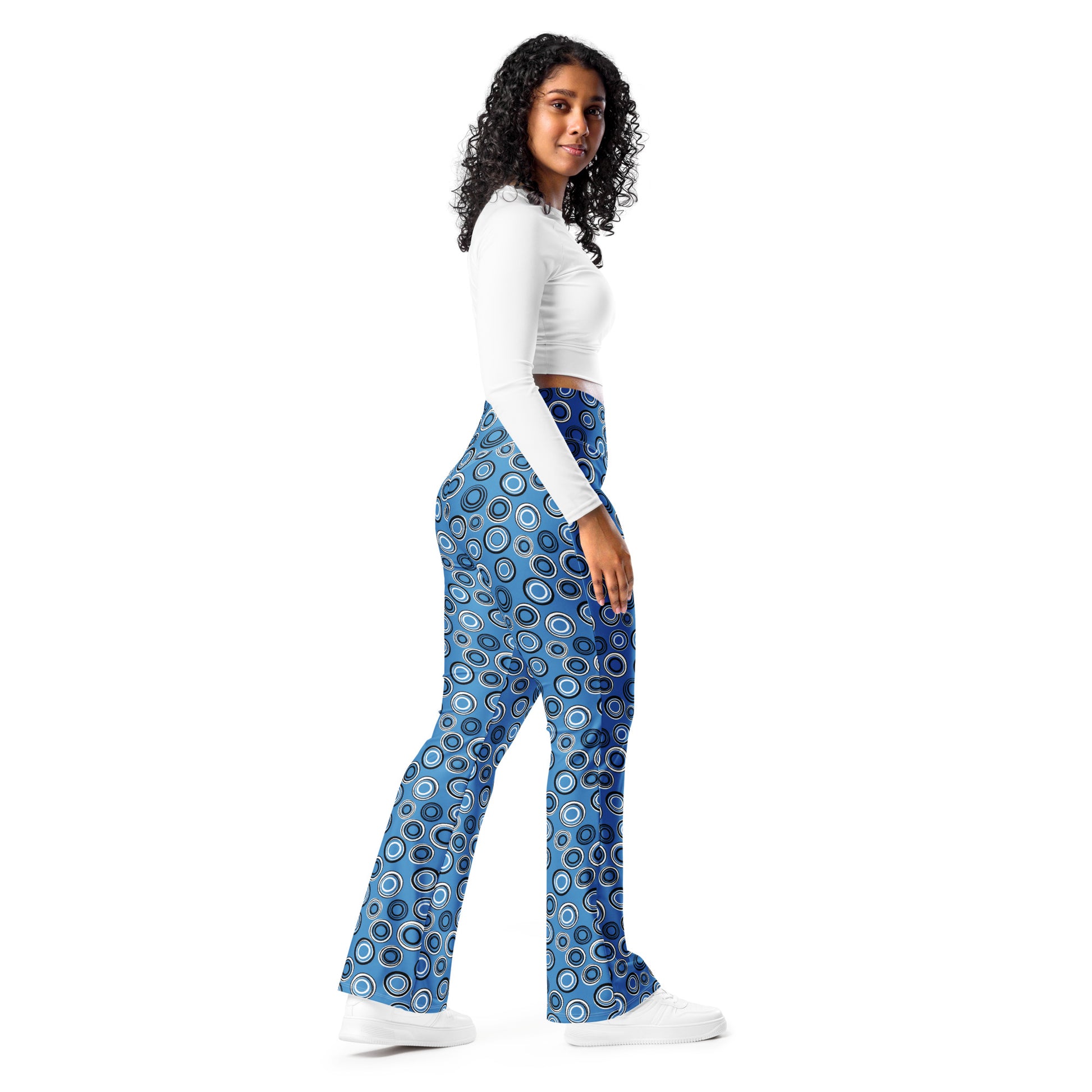 A woman modeling a pair of blue flared pants with a circular concentric pattern, paired with a white long-sleeve crop top and white sneakers, set against a plain white background. Beautiful Celestial Planetary Orbit Pattern Flare Leggings Activewear
