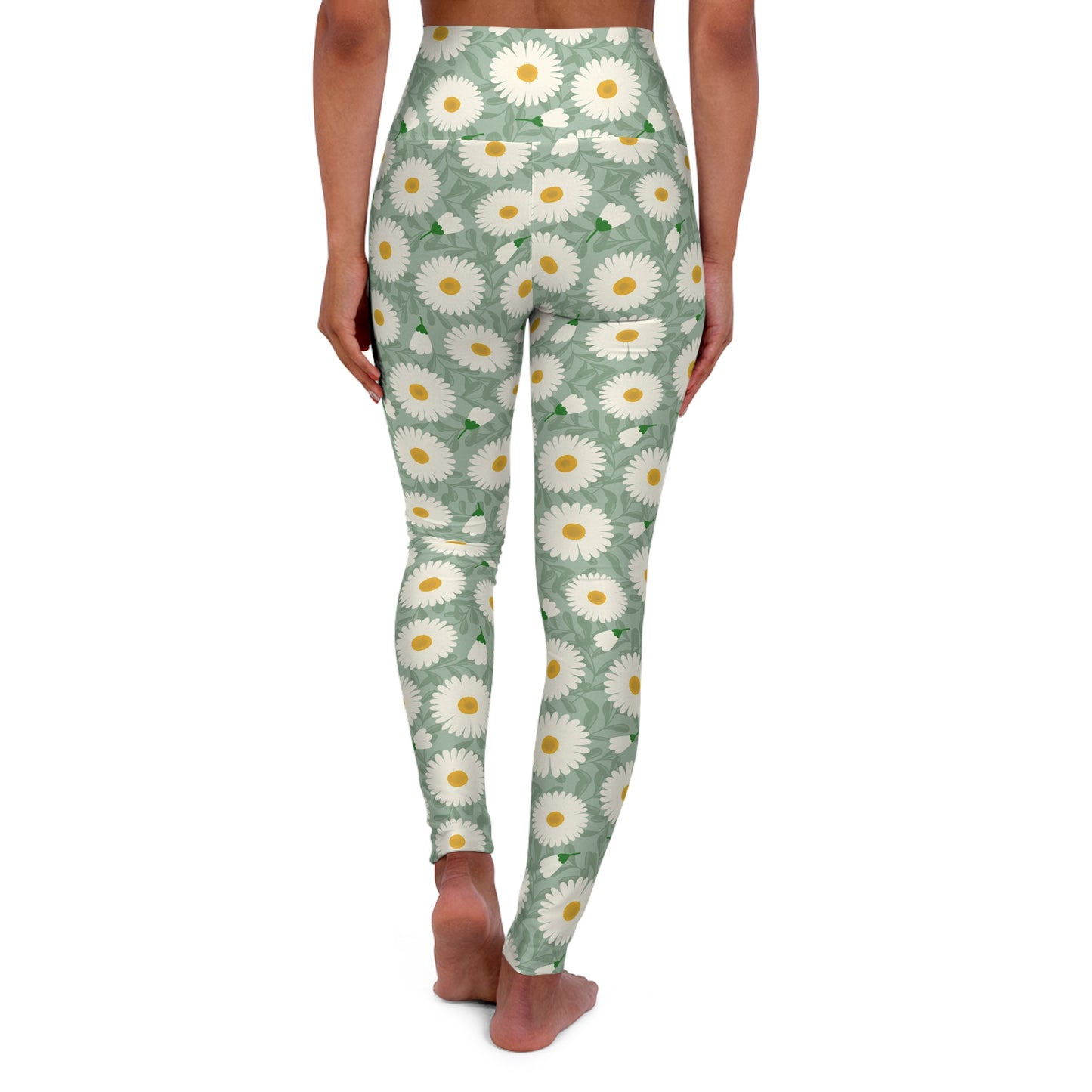 A person shown from the back wearing high-waisted leggings with an allover daisy print on a sage green background, standing barefoot against a plain white studio background.