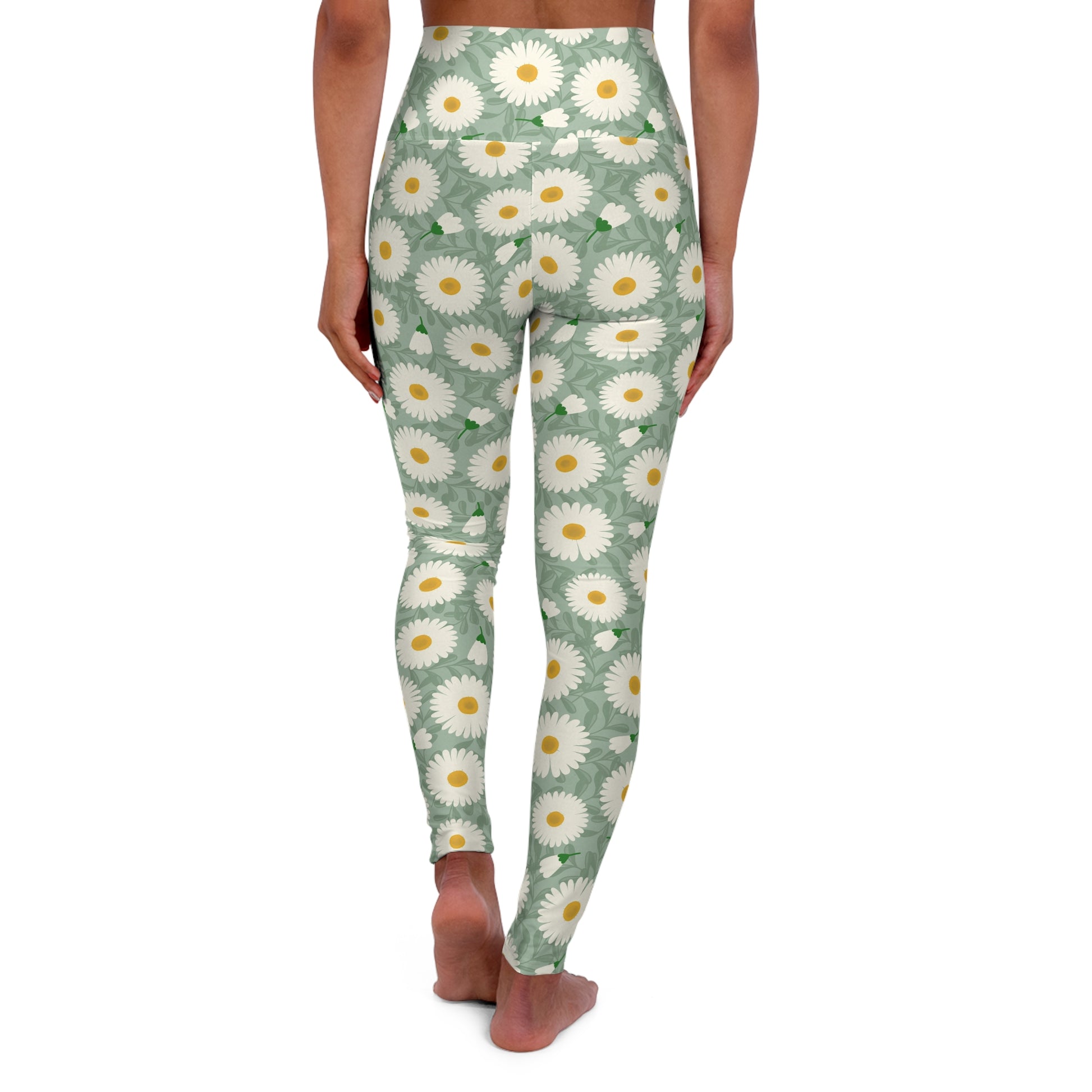 A person shown from the back wearing high-waisted leggings with an allover daisy print on a sage green background, standing barefoot against a plain white studio background.