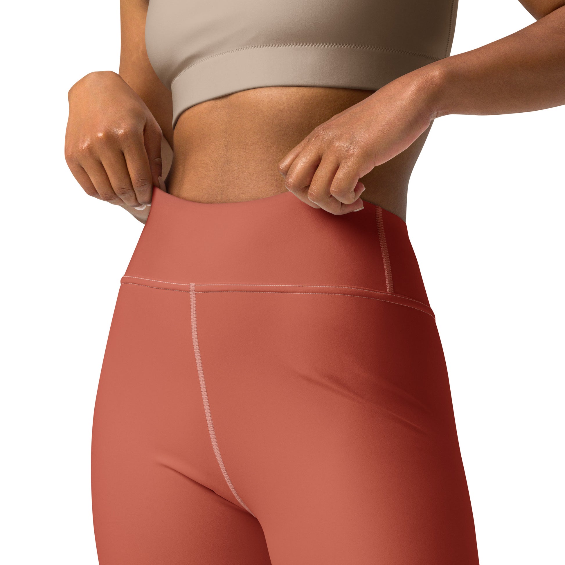 Close-up of a model wearing high-waisted terracotta pink athletic leggings with a beige sports bra against a white background. Bold Stretchy Yoga Leggings with Solid Dark Coral Unique Design