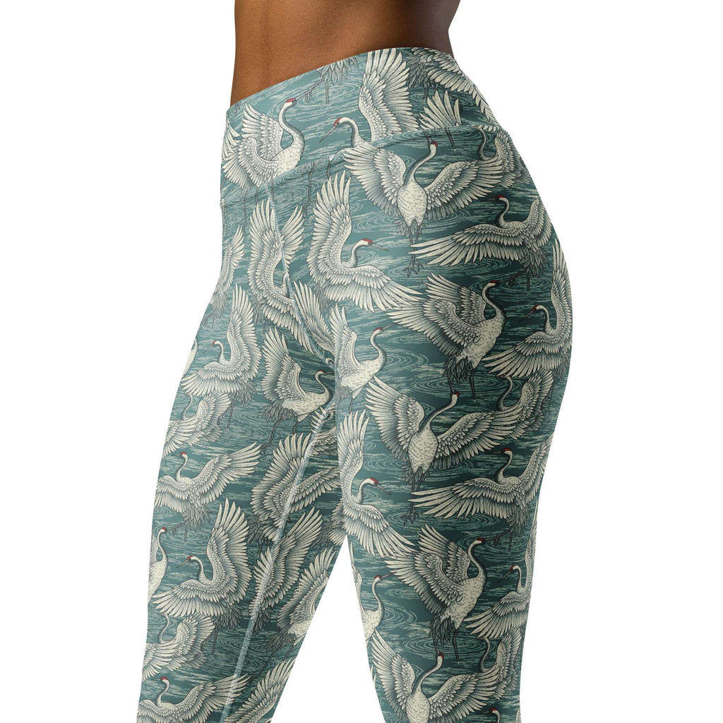 Side view of a person wearing high-waisted leggings with an allover print of white cranes over a textured teal background, against a plain white studio backdrop. Chic Minimalist Bold Yoga Leggings in Artistic Crane Dance Print