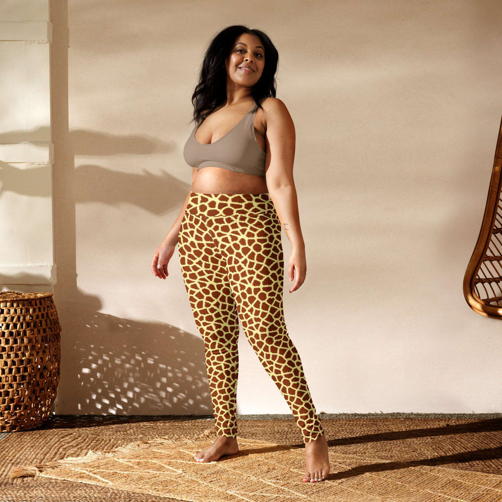 A woman modeling high-waisted leggings with a brown and beige giraffe print pattern, paired with a taupe sports bra, standing in a sunlit room with a textured beige wall and woven decor. Chic Stylish Giraffe Print Yoga Pants for Active Wear