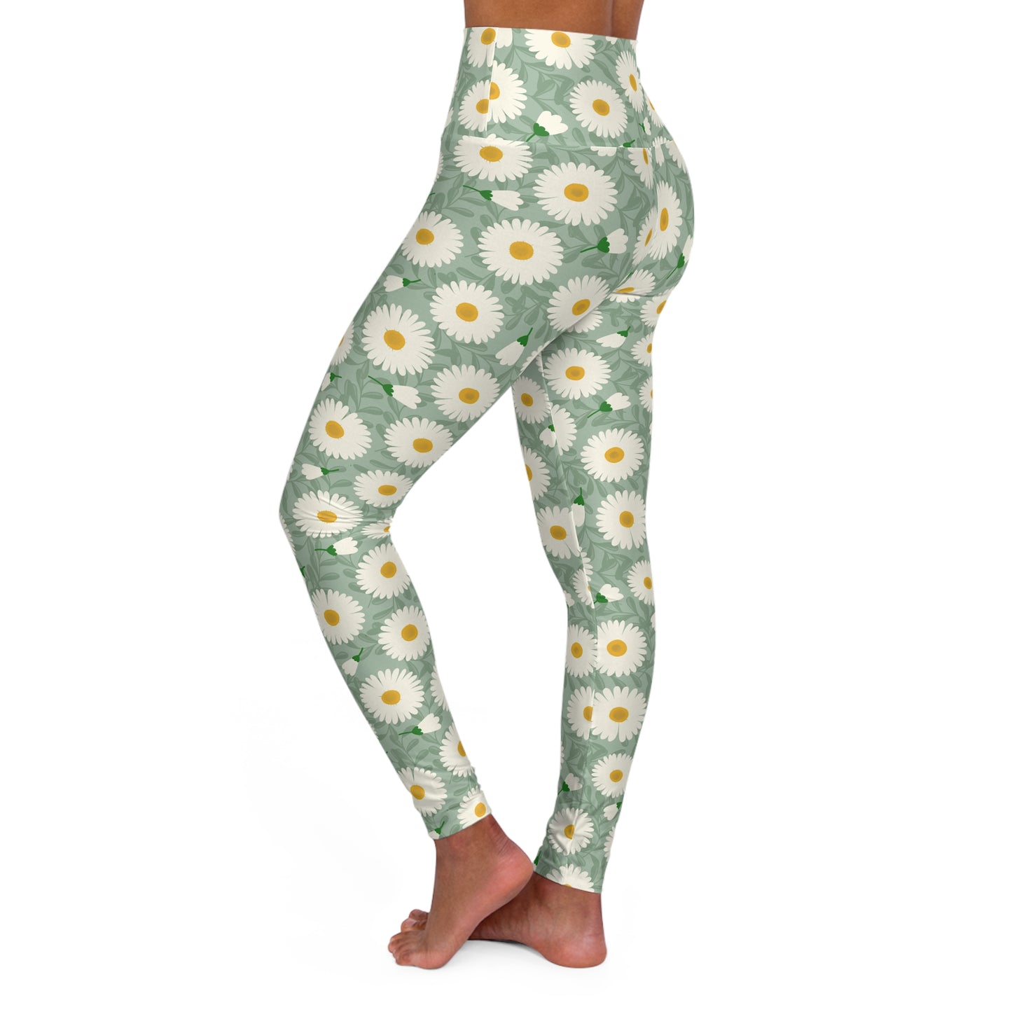 A person modeling high-waisted leggings with a sage green background and a white daisy floral pattern with yellow centers, shown from the waist down against a plain white background.