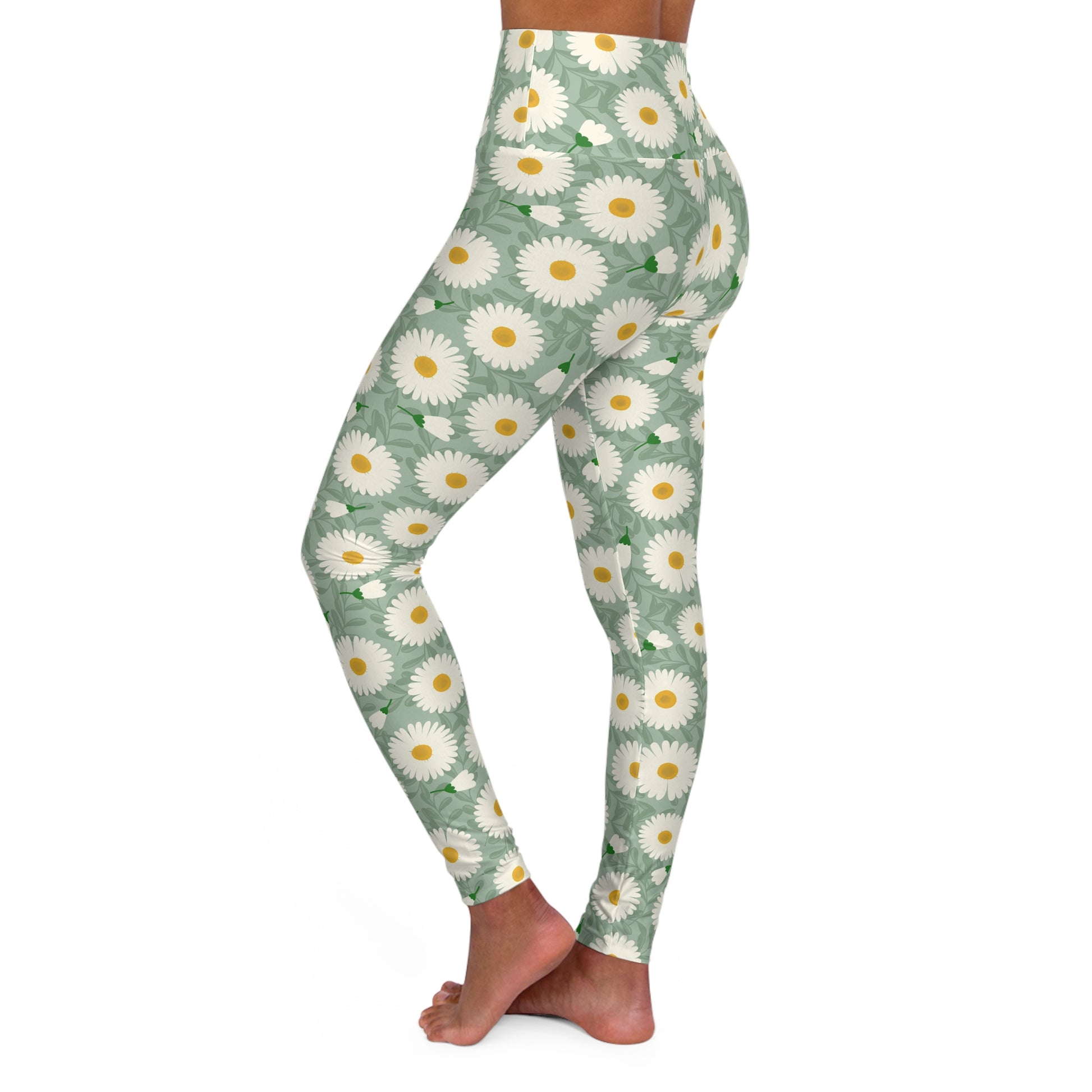 A person modeling high-waisted leggings with a sage green background and a white daisy floral pattern with yellow centers, shown from the waist down against a plain white background.