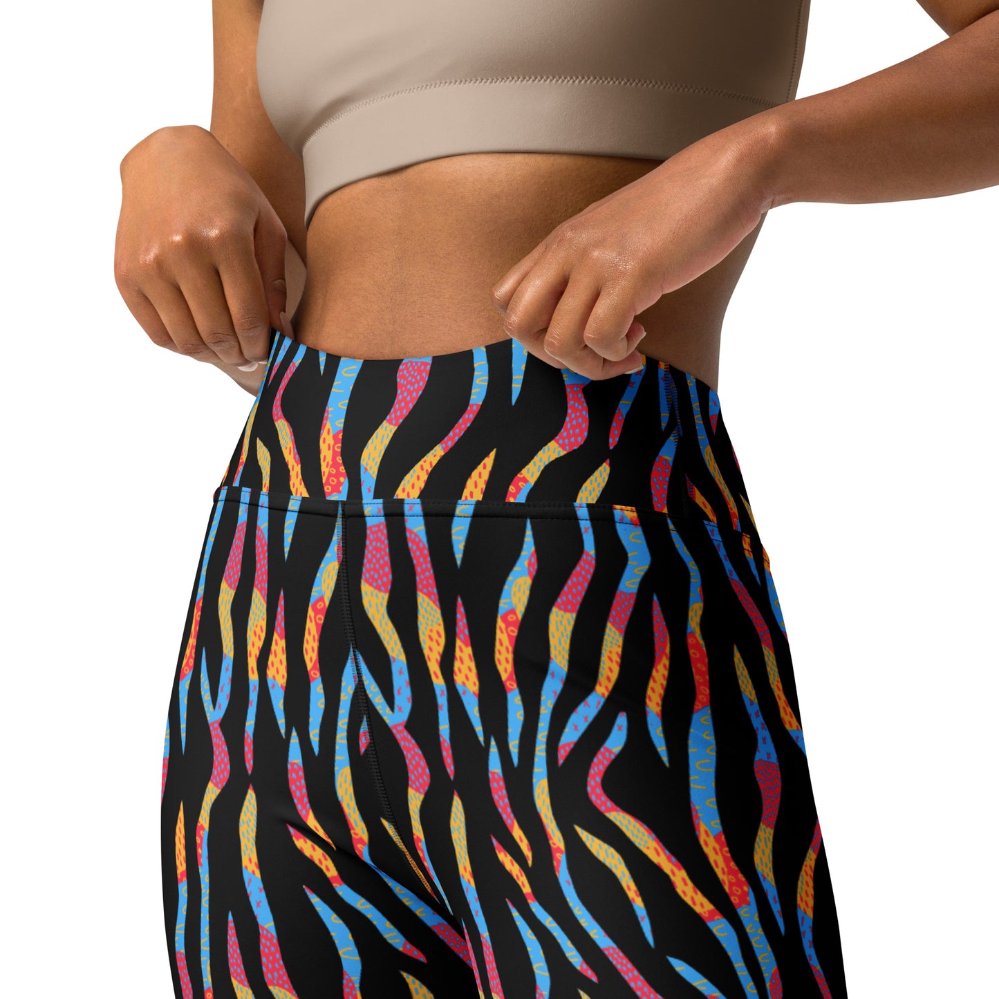 Close-up of a model wearing high-waisted athletic leggings with a black base and a colorful abstract wavy pattern in blue, pink, orange, and yellow, paired with a beige sports bra against a white background. Durable Colorful Zebra Print Yoga Leggings for Active Wear