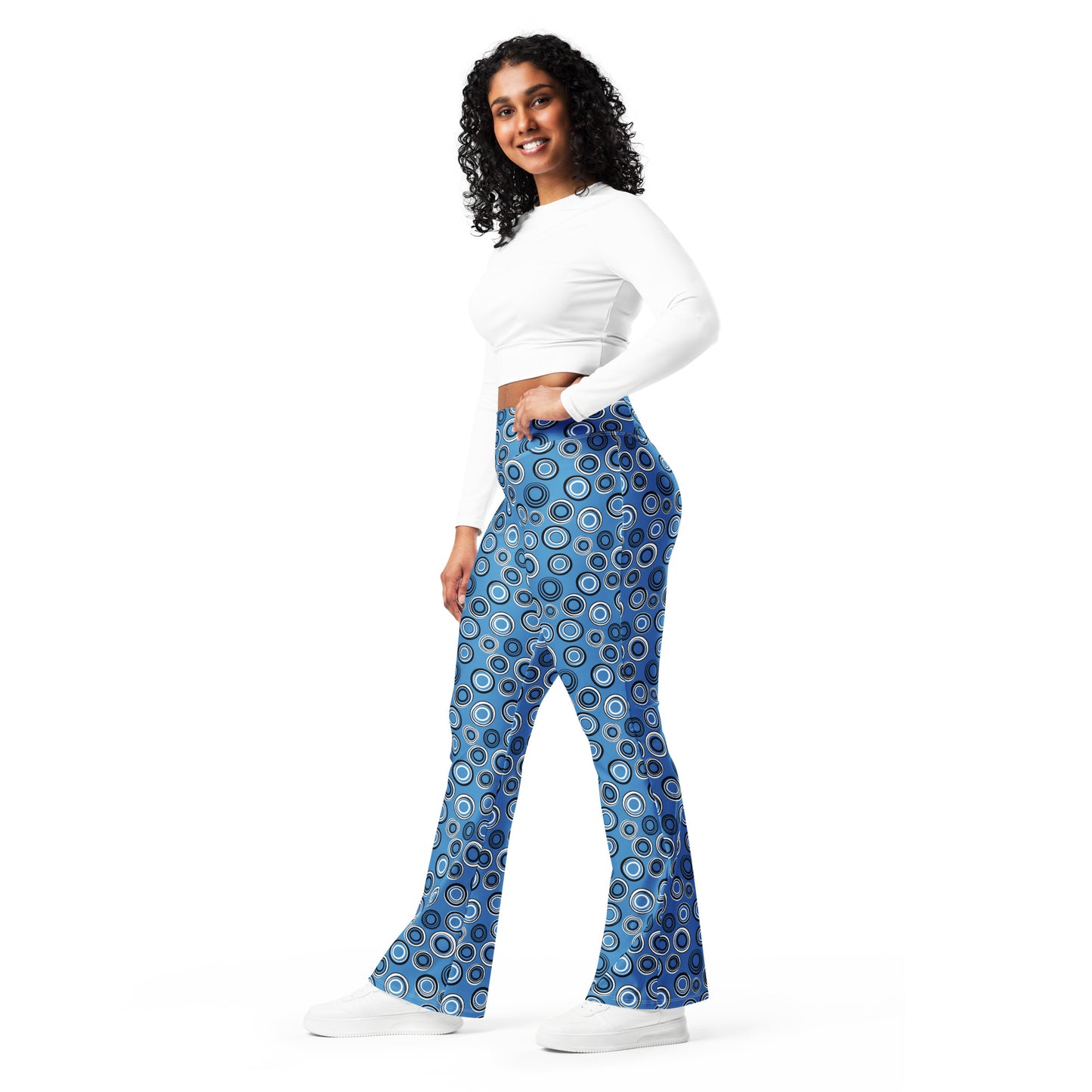 A woman modeling a pair of high-waisted, wide-leg pants with a blue, white, and black concentric circle pattern, paired with a white long-sleeve crop top and white sneakers, set against a plain white background. Elegant Celestial Planetary Orbit Pattern Flare Leggings Activewear