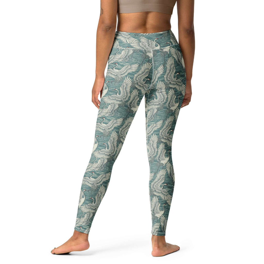 A model from the waist down wearing high-waisted leggings with a teal and off-white phoenix pattern, standing against a plain white background. Fashionable Minimalist Bold Yoga Leggings in Artistic Crane Dance Print
