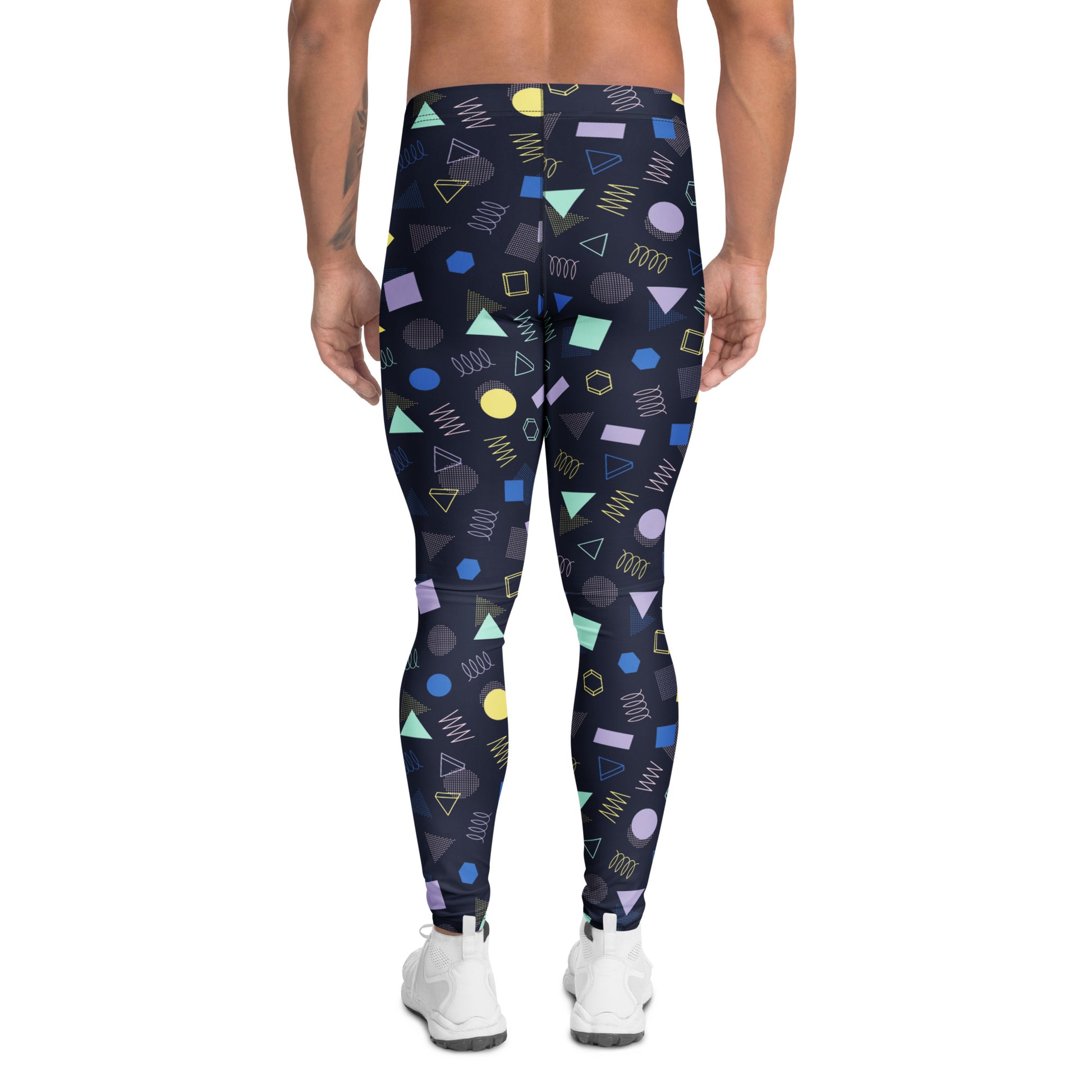 A person modeling high-waisted leggings with a colorful geometric pattern on a plain white studio background. The leggings have a dark base with shapes in blue, yellow, green, purple, and orange, and the model is wearing white sneakers. Minimalist Bold Aesthetic Geometric Memphis Men's Leggings Activewear