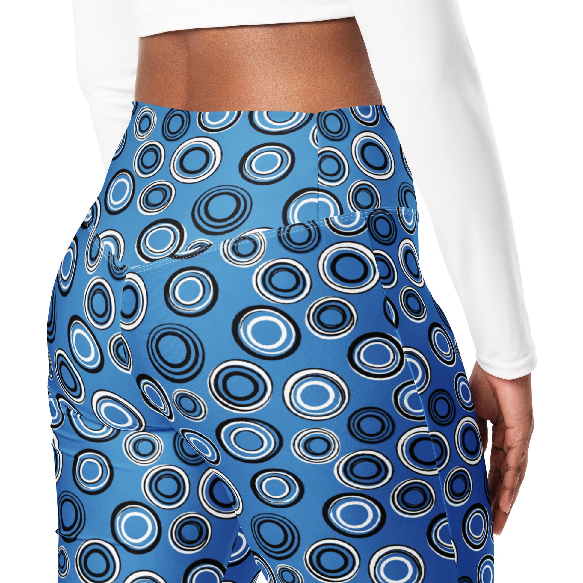 A close-up of a person wearing high-waisted blue leggings with a bold black, white, and light blue concentric circle pattern, paired with a white long-sleeve top against a plain white background. Pretty Celestial Planetary Orbit Pattern Flare Leggings Activewear
