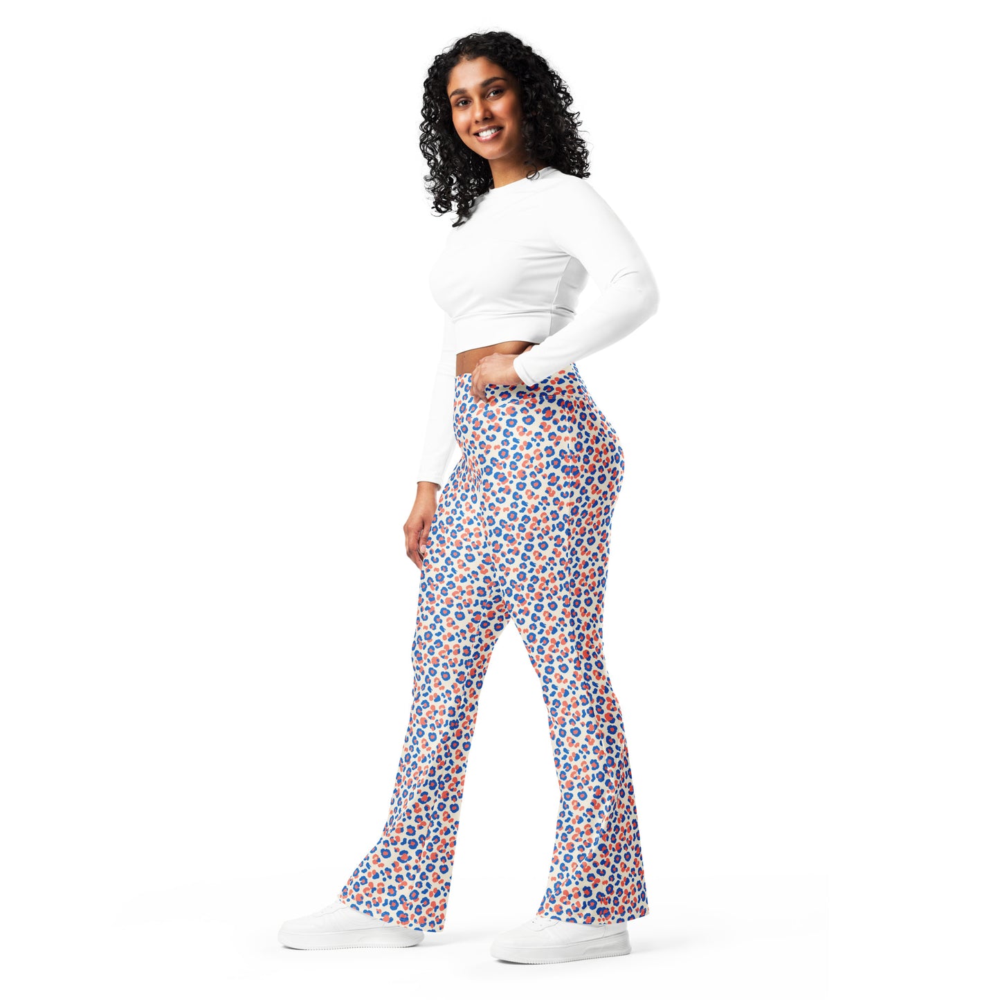 A woman modeling a pair of high-waisted, flared pants with a colorful geometric pattern in blue, orange, and white, paired with a white long-sleeve crop top and white sneakers against a solid white background. Stylish Colorful Leopard Print Flare Leggings Active Wear