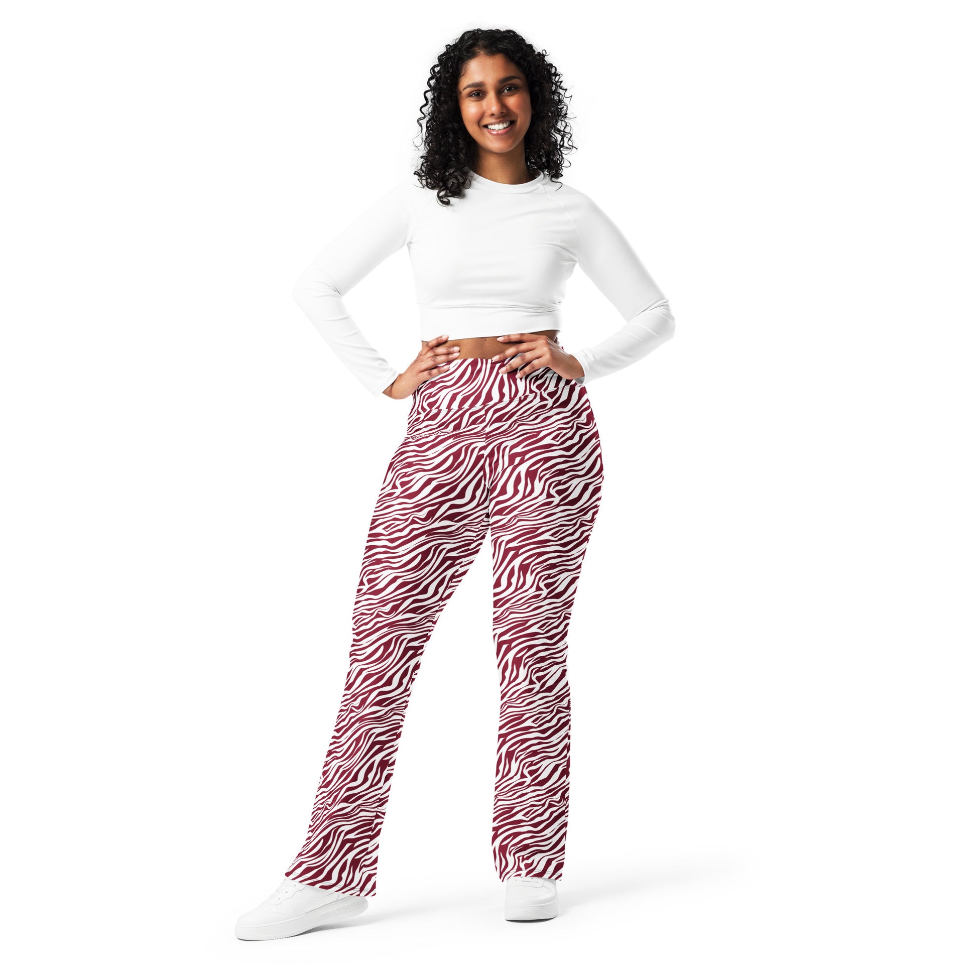 A woman modeling high-waisted flare pants with a red and white zebra print, paired with a white long-sleeve crop top and white sneakers, against a solid white background. Stylish Comfortable Bold Red Zebra Print Flare Leggings