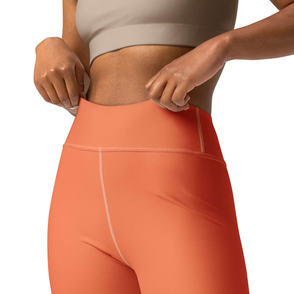 Close-up of a model wearing high-waisted coral pink leggings with a white circular pattern, paired with a beige sports bra against a white background. Top Rated Chic Comfortable Yoga Pants in Solid Coral Shade for Activewear