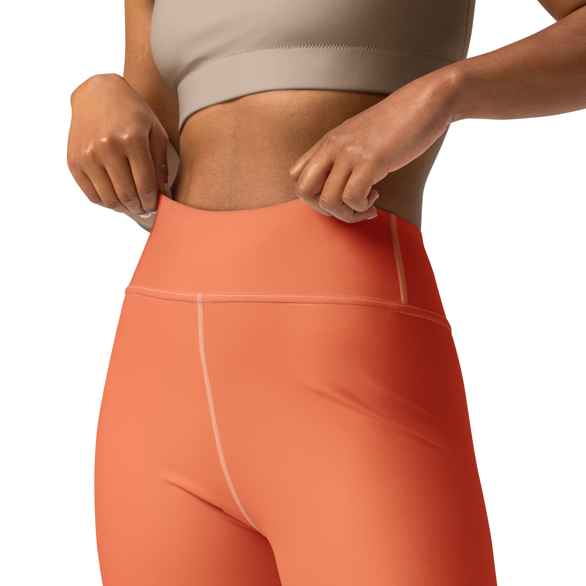 Close-up of a model wearing high-waisted coral pink leggings with a white circular pattern, paired with a beige sports bra against a white background. Top Rated Chic Comfortable Yoga Pants in Solid Coral Shade for Activewear