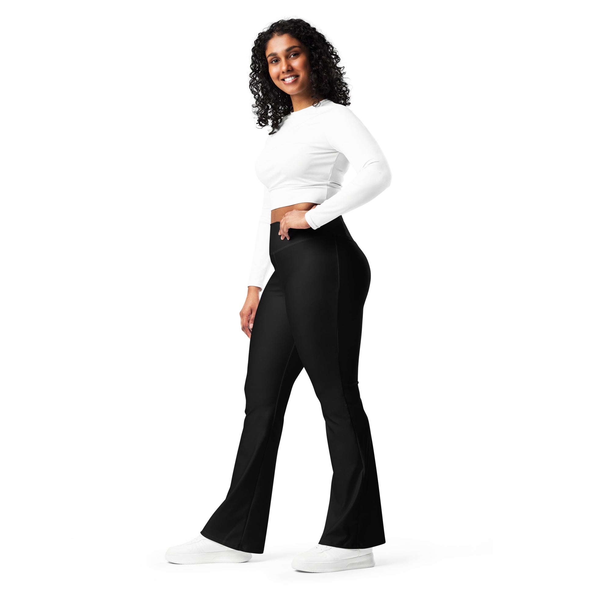 A woman modeling black flared pants with a white long-sleeve crop top and white sneakers, standing against a solid white background. Trendy Minimalist Solid Black Flare Leggings for Activewear