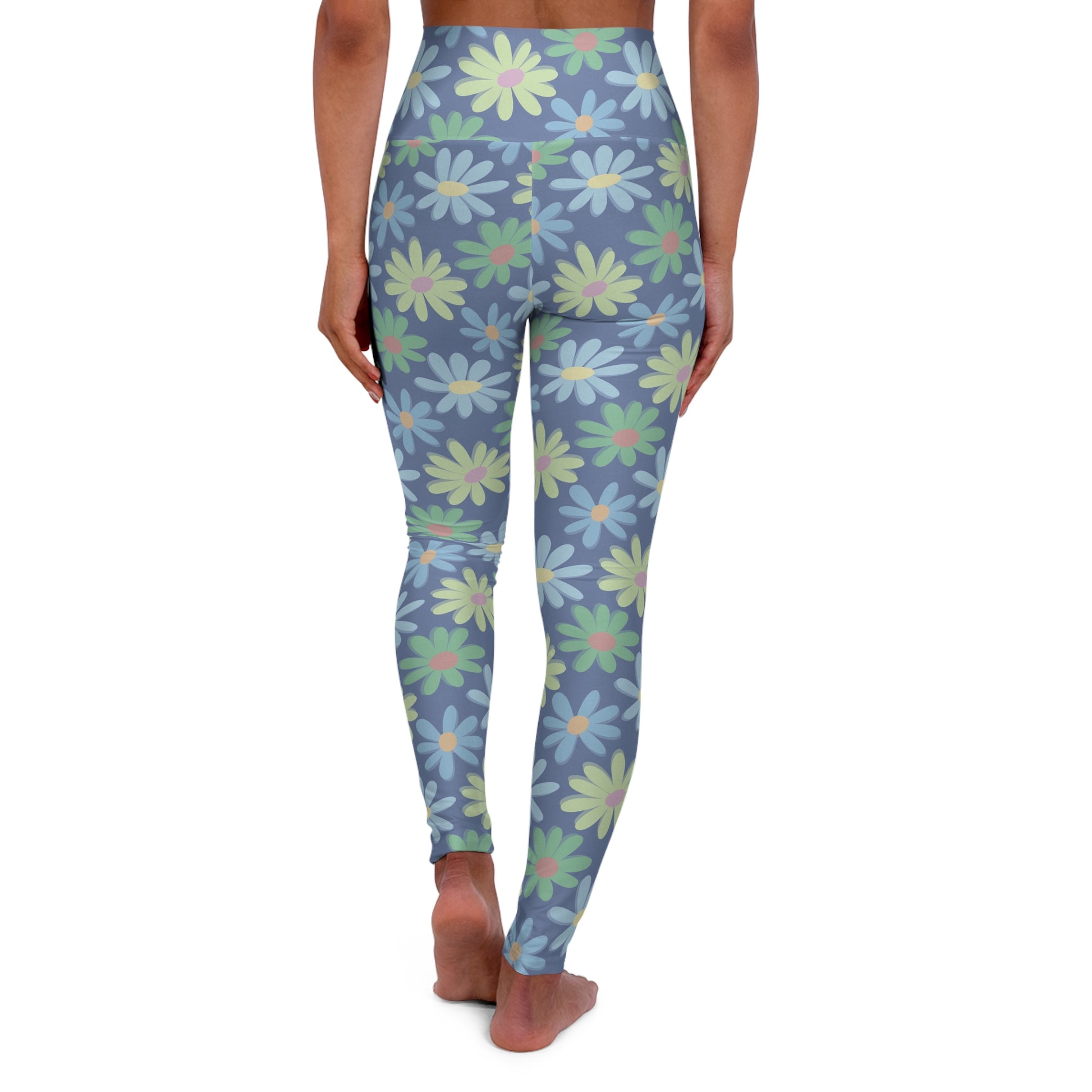A person shown from the back wearing high-waisted leggings with a blue-gray base and a repeating daisy pattern in light green, white, and soft yellow, standing barefoot against a plain white background.