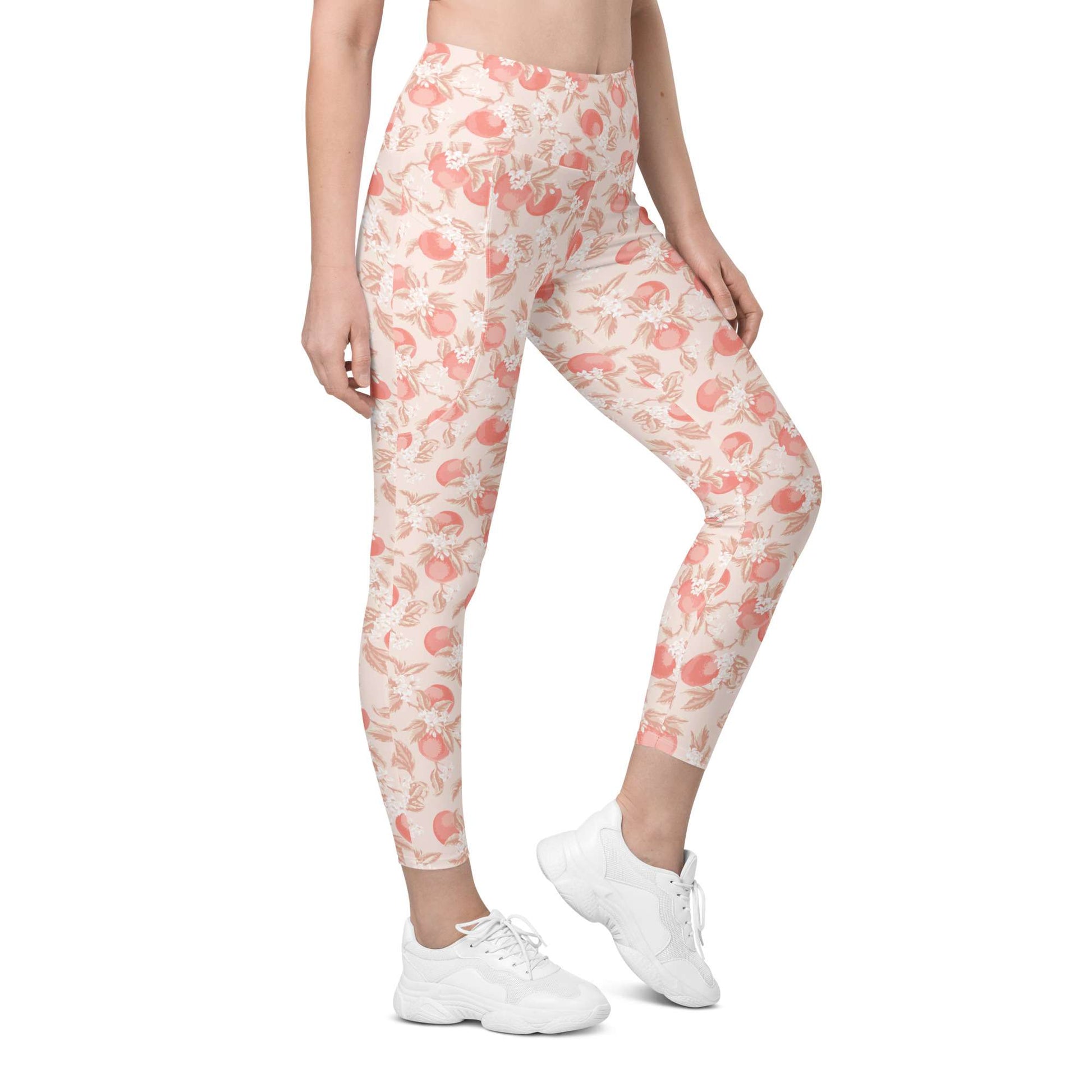 A model wearing high-waisted leggings with a peach and pink floral pattern on a cream background, paired with white sneakers, shown against a plain white studio background. Artistic Ditsy Floral Print Leggings with Pockets Activewear Artistic Stylized Ditsy Floral Pattern with Blue and Orange Botanical Motifs Leggings with Pockets Activewear Shop Artistic Ditsy Floral Print Leggings with Pockets, designed for bold outfits, flexible movement, and convenient everyday storage.